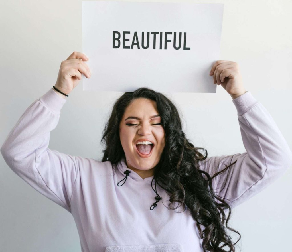 Woman in a small fat body holds sign saying "Beautiful"