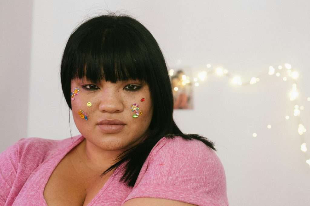 A woman confidently looks directly at the camera with sparkly stickers on her face