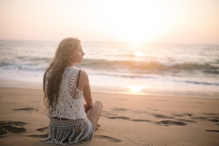 A woman sits at the beach, looking thoughtfully into the distance