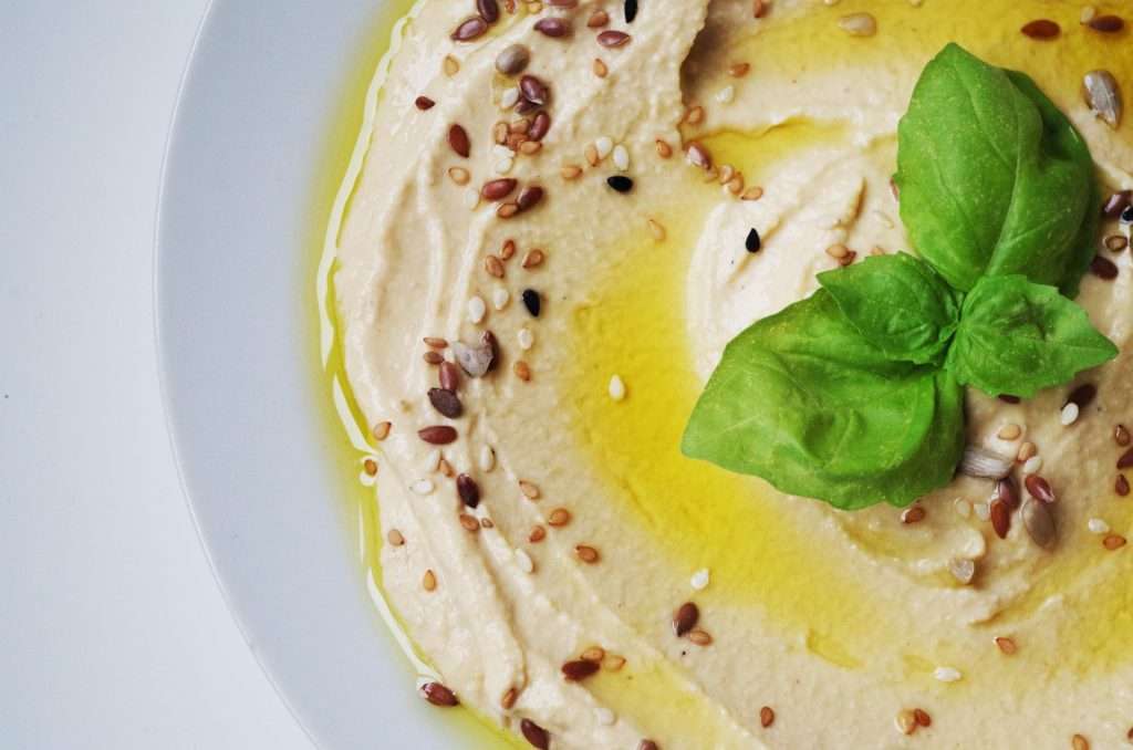 a beautifully presented plate of hummus, sprinkled with olive oil and various seeds, and topped with a sprig of herbs