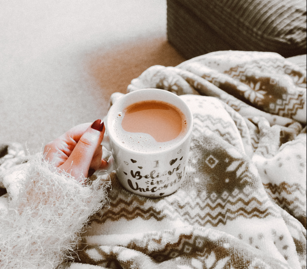 a cozy POV picture of someone holding a mug, covered in a super soft blanket