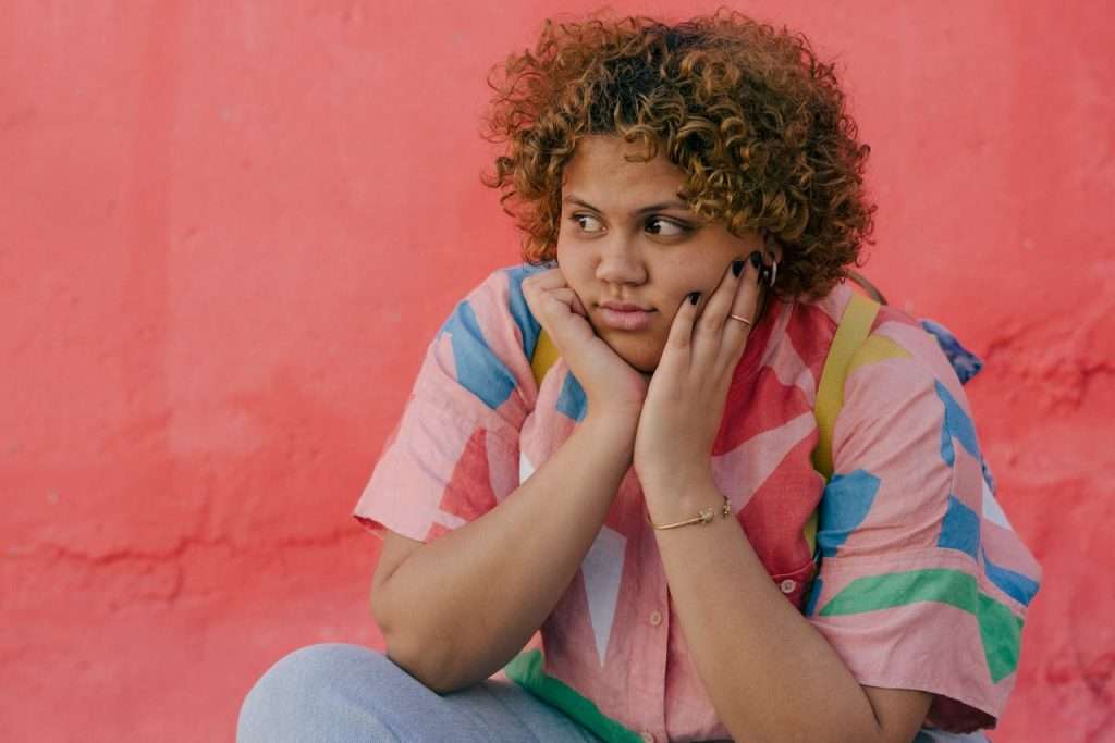 A woman sits near a colorful wall, looking off into the distance