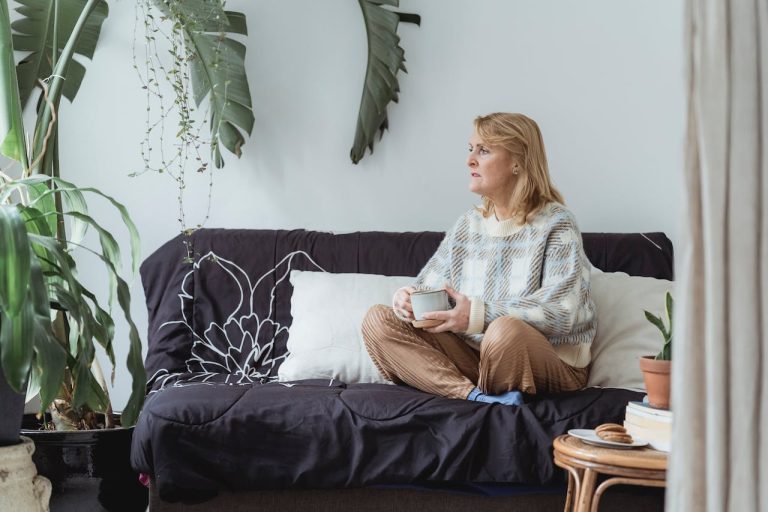 Woman sits on couch holding a mug and looking off in the distance